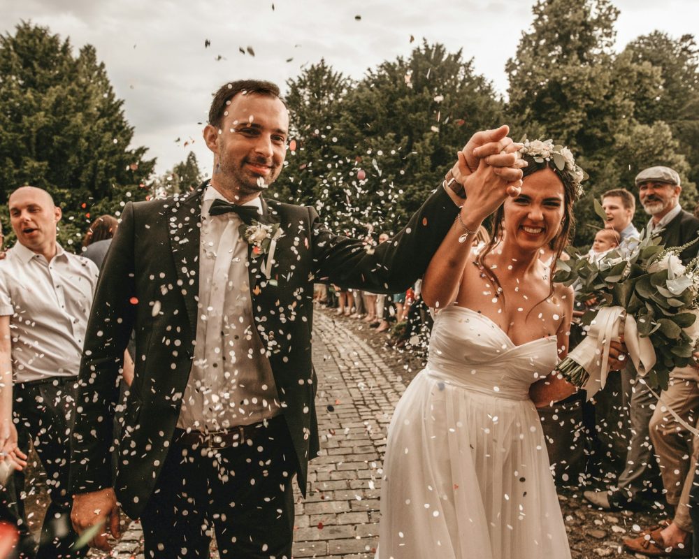 Front view of happy newlywed couple walking through a gauntlet of wedding guests.